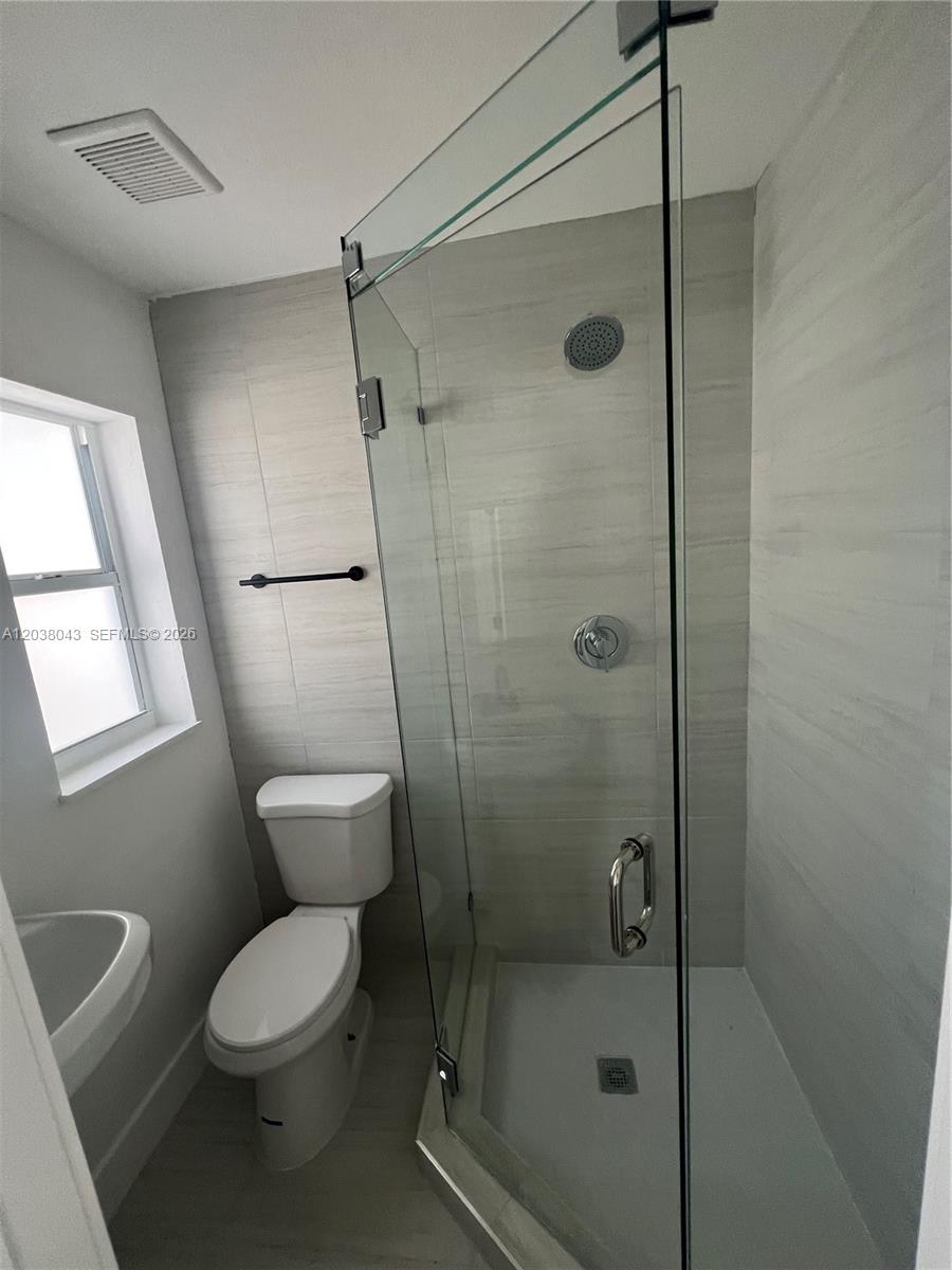 A bathroom features a glass-enclosed shower, a white toilet, and light-colored wall tiles — 1706 Arthur St, Hollywood FL 33020, HOLLYWOOD, FL