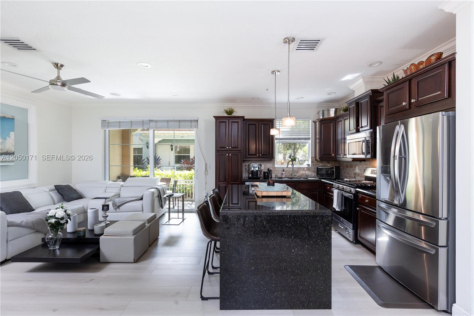An open-concept kitchen with dark wood cabinets and a granite island overlooks a living area — 3300 NW 126th Ter, Sunrise FL 33323, SUNRISE, FL