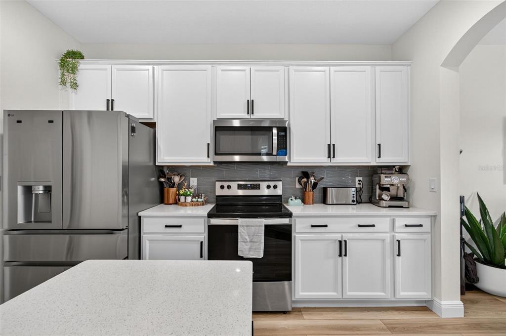 A modern kitchen features white cabinets, stainless steel appliances, and a light-colored quartz countertop — 2 RIDGE ROAD, PALM COAST, FL
