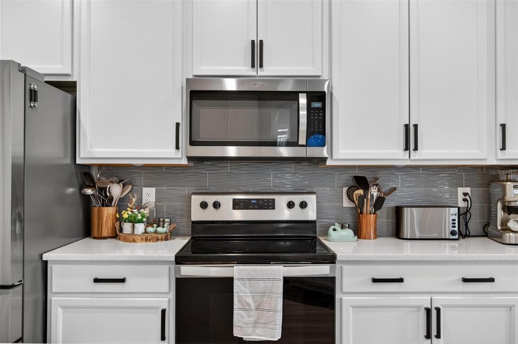 A kitchen features white cabinets, stainless steel appliances, and a gray horizontal tile backsplash — 2 RIDGE ROAD, PALM COAST, FL