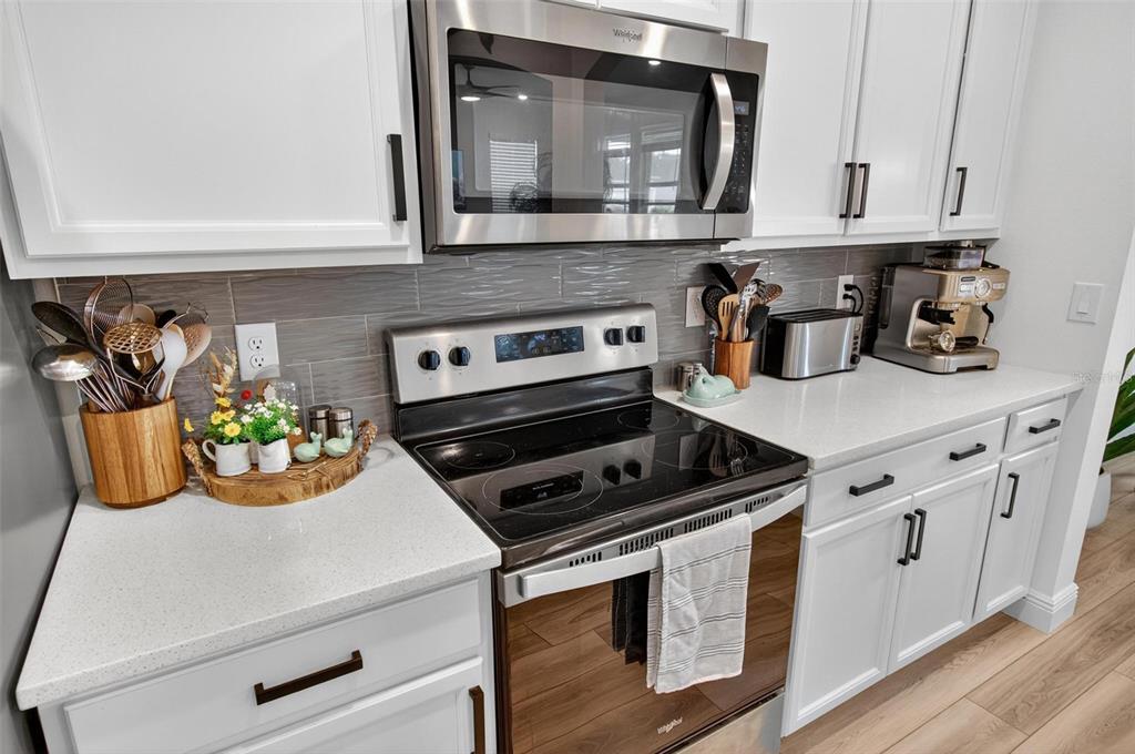 A kitchen features white cabinets, stainless steel appliances, a glass stovetop, and gray tile backsplash — 2 RIDGE ROAD, PALM COAST, FL