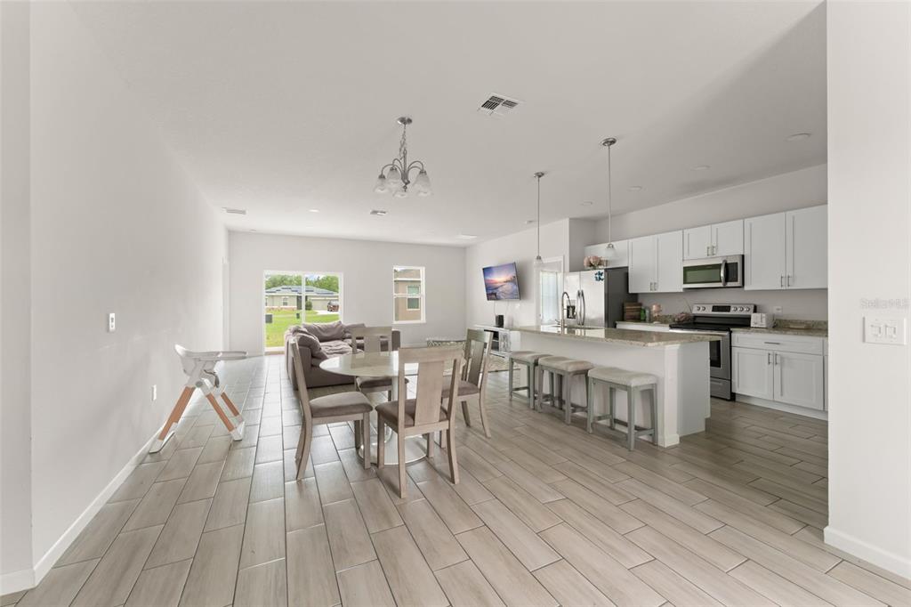 An open-concept kitchen and dining area with white cabinets, granite countertops, and light tile flooring — 274 ELM COURT, KISSIMMEE, FL