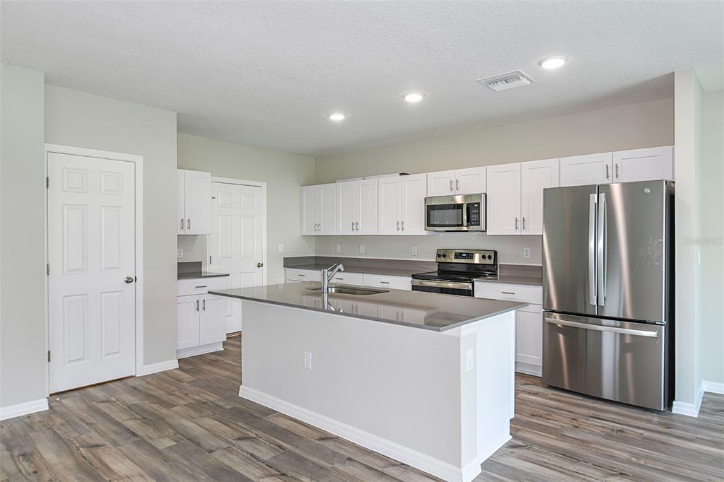 A kitchen features white cabinets, stainless steel appliances, a center island, and wood-look flooring — 1739 VANILLA STREET, LAKE HAMILTON, FL
