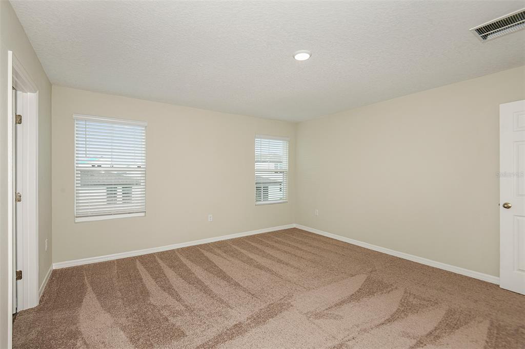 An empty bedroom with beige walls, tan carpet, two windows with blinds, and white doors — 1739 VANILLA STREET, LAKE HAMILTON, FL