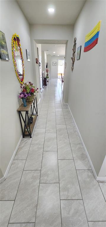 A long hallway with light gray tile flooring leads toward a bright, open living area — 1823 SPRING SHOWER CIR, KISSIMMEE, FL