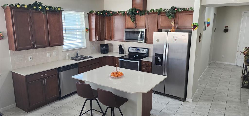 A kitchen features dark wood cabinets, stainless steel appliances, a white island, and tiled floors — 1823 SPRING SHOWER CIR, KISSIMMEE, FL