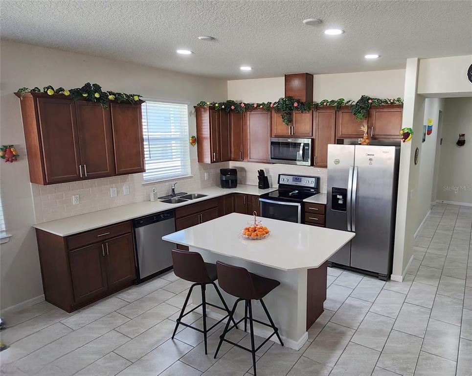 A kitchen features dark wood cabinets, white countertops, stainless steel appliances, and a central island — 1823 SPRING SHOWER CIR, KISSIMMEE, FL
