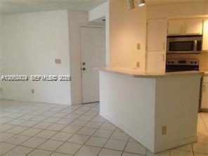 A white kitchen with a breakfast bar overlooks a tiled living area near an entrance — 3380 N Pinewalk Dr N # 1116, Margate FL 33063, MARGATE, FL