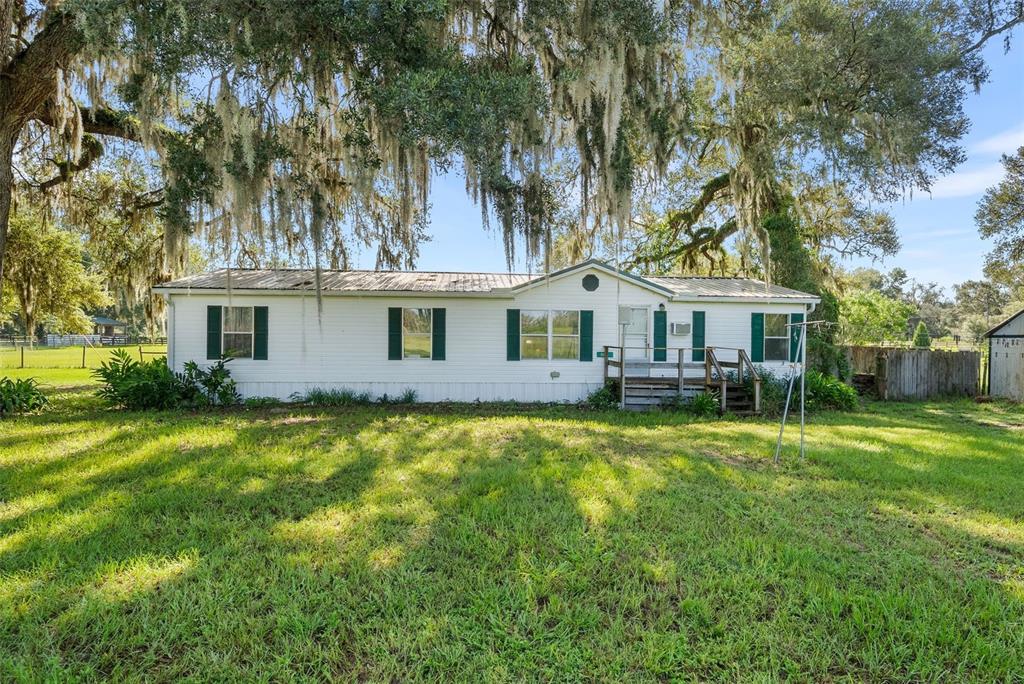 A white single-wide mobile home with dark green shutters sits on a grassy lot — 360 SE 30TH AVENUE, TRENTON, FL