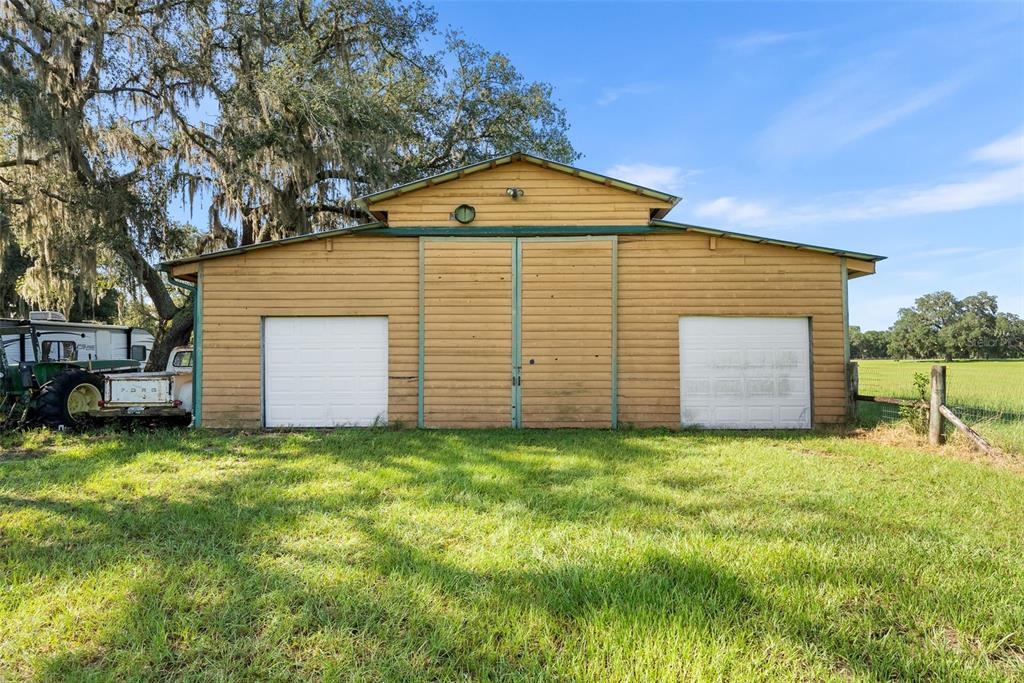 A yellow barn with two white garage doors sits in a grassy field under trees — 360 SE 30TH AVENUE, TRENTON, FL
