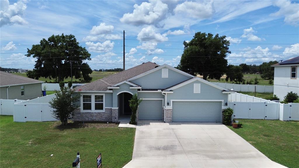 A light blue single-story house with a stone facade, three-car garage, and white vinyl fencing — 4710 SW 65TH PLACE, OCALA, FL