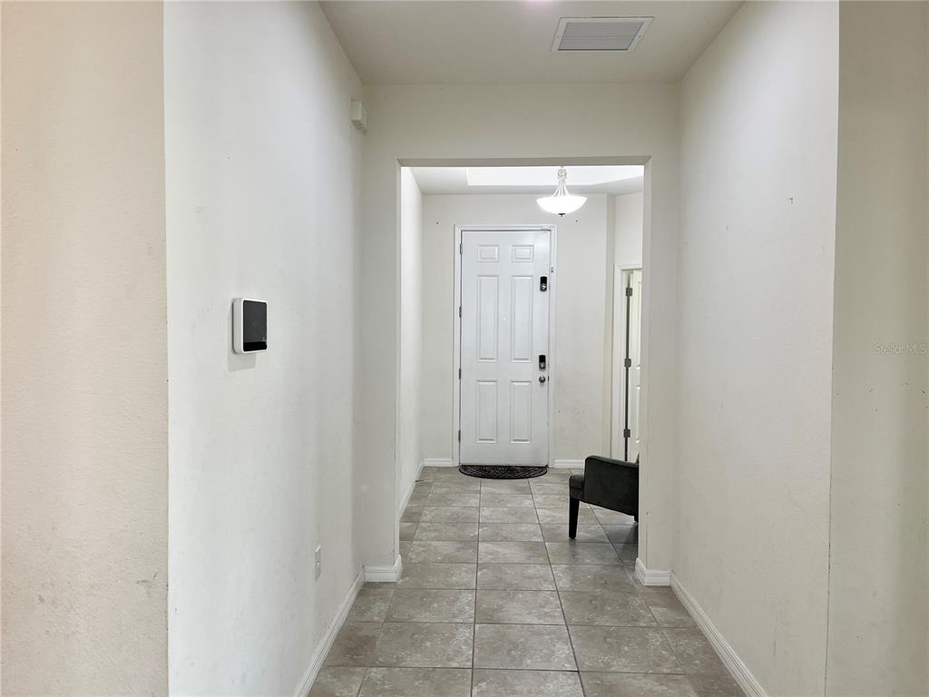 A tiled entryway features a white front door, a wall-mounted thermostat, and a small chair — 4710 SW 65TH PLACE, OCALA, FL