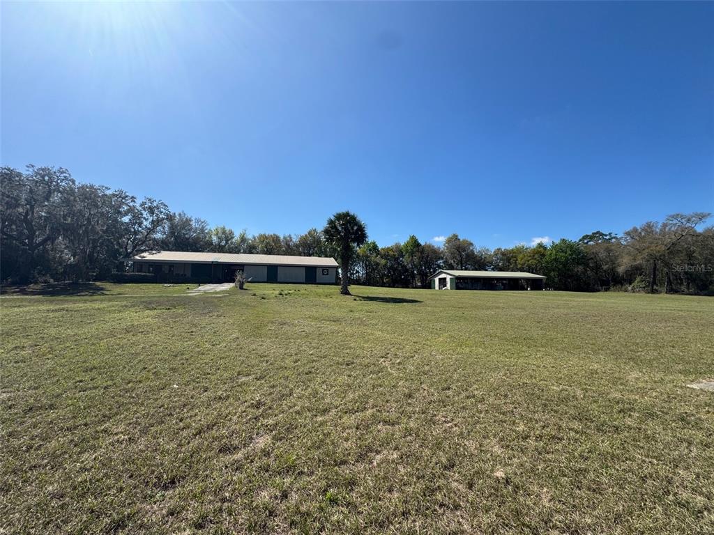 A wide, grassy field leads to a long, single-story house and a separate detached structure — 1065 S MASSACHUSETTS AVENUE, DELAND, FL