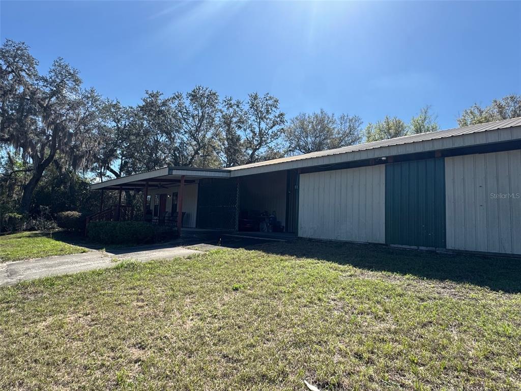 A metal-sided building with a covered porch and an attached carport sits on a lawn — 1065 S MASSACHUSETTS AVENUE, DELAND, FL