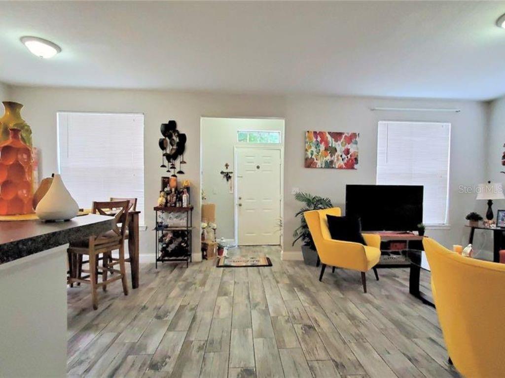 A living room features wood-look tile flooring, yellow accent chairs, and a front entryway door — 6025 WESTGATE DRIVE UNIT 2511, ORLANDO, FL