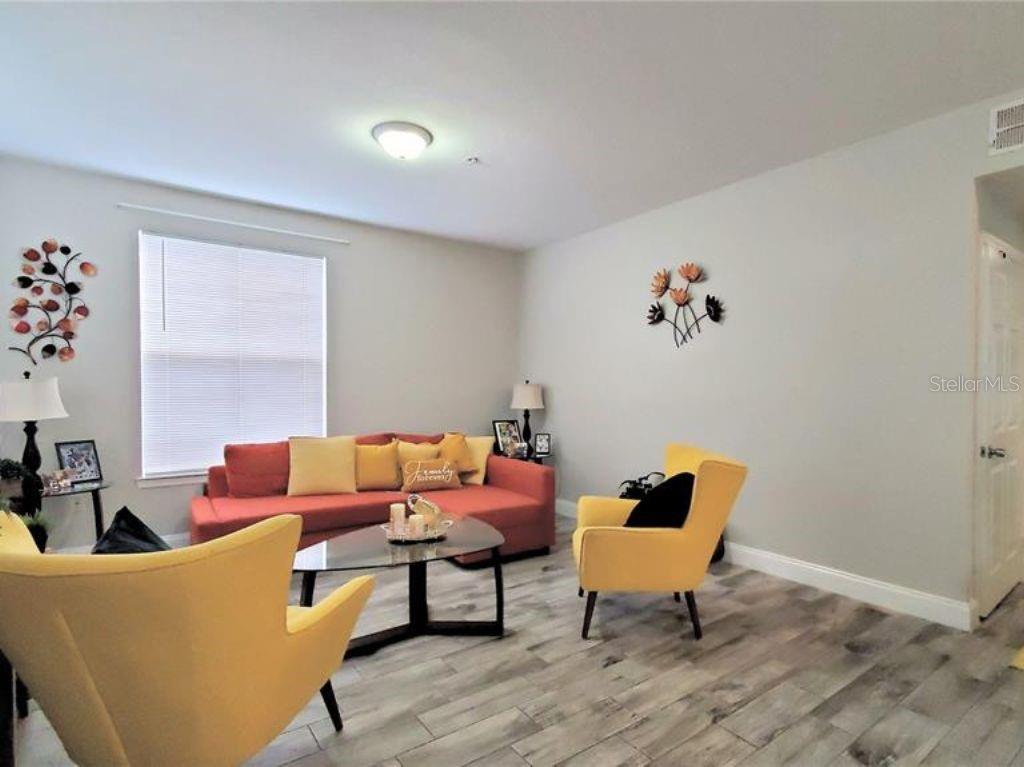 A living room features a coral sofa, two yellow armchairs, and wood-look tile flooring — 6025 WESTGATE DRIVE UNIT 2511, ORLANDO, FL