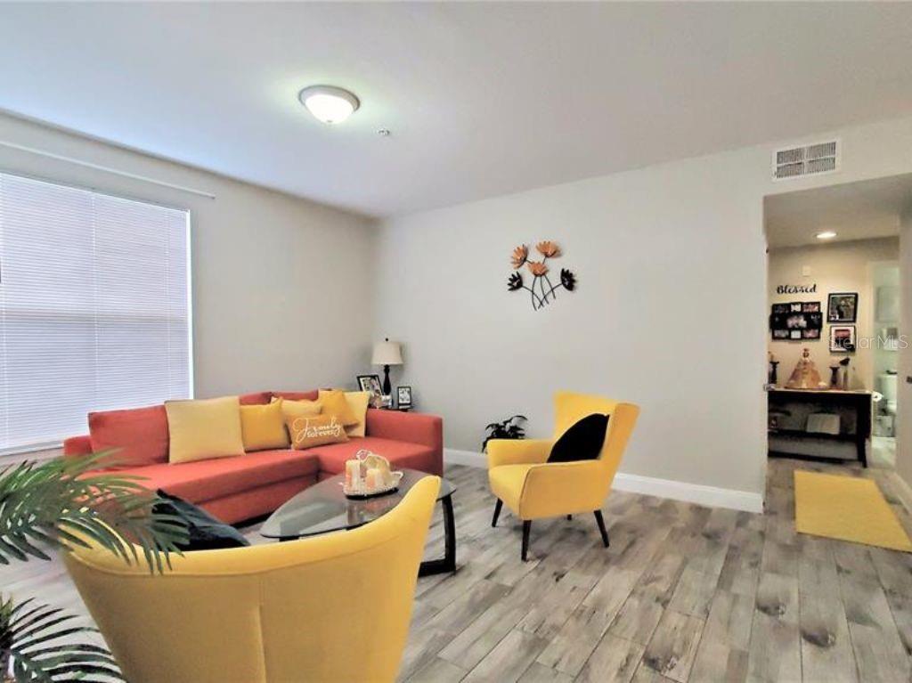 A living room features a coral sofa, two yellow armchairs, and light wood-look flooring — 6025 WESTGATE DRIVE UNIT 2511, ORLANDO, FL