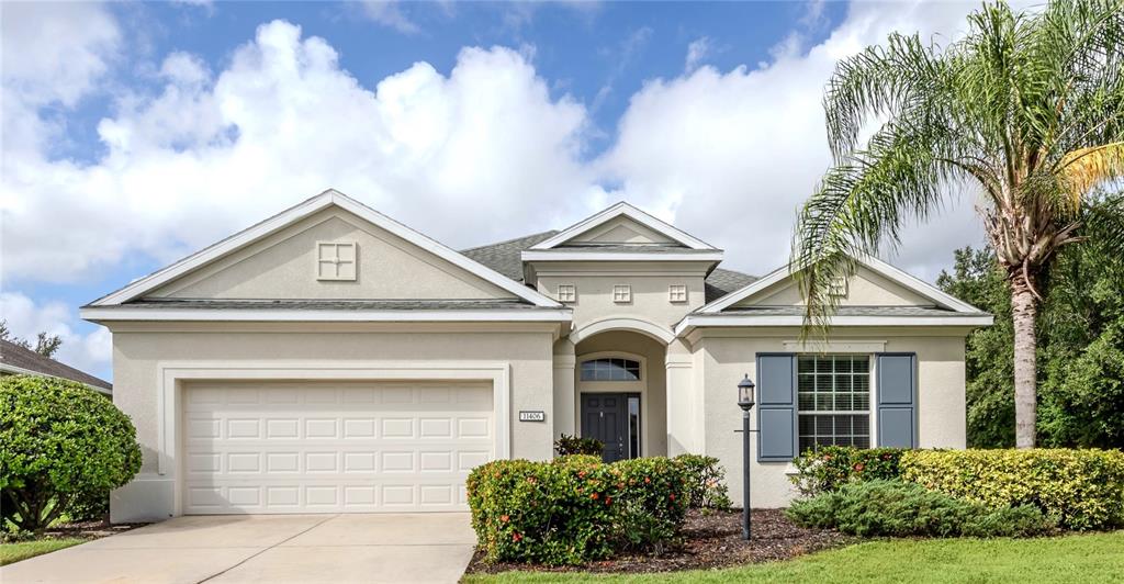 A single-story suburban house with a two-car garage, beige stucco exterior, and a palm tree — 11406 BELVEDERE TERRACE, BRADENTON, FL