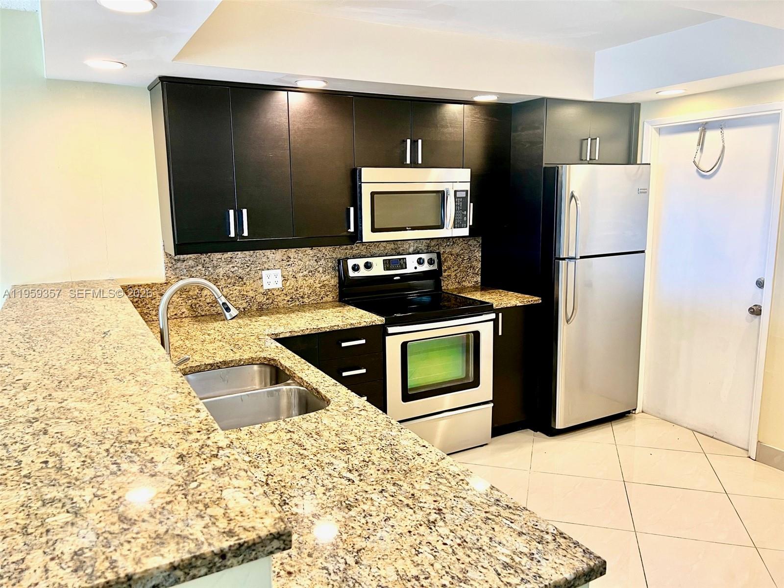 A kitchen features dark cabinets, granite countertops, stainless steel appliances, and light tile flooring — 2940 N Course Dr # 910, Pompano Beach FL 33069, POMPANO BEACH, FL