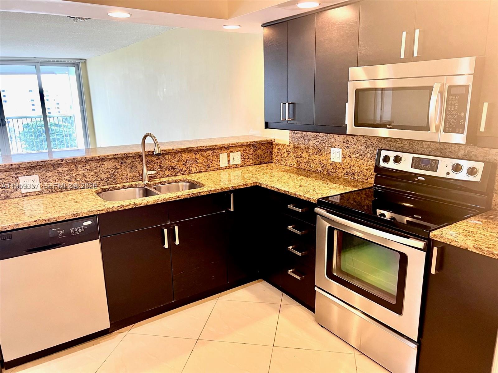A kitchen features dark cabinets, granite countertops, stainless steel appliances, and a tile floor — 2940 N Course Dr # 910, Pompano Beach FL 33069, POMPANO BEACH, FL