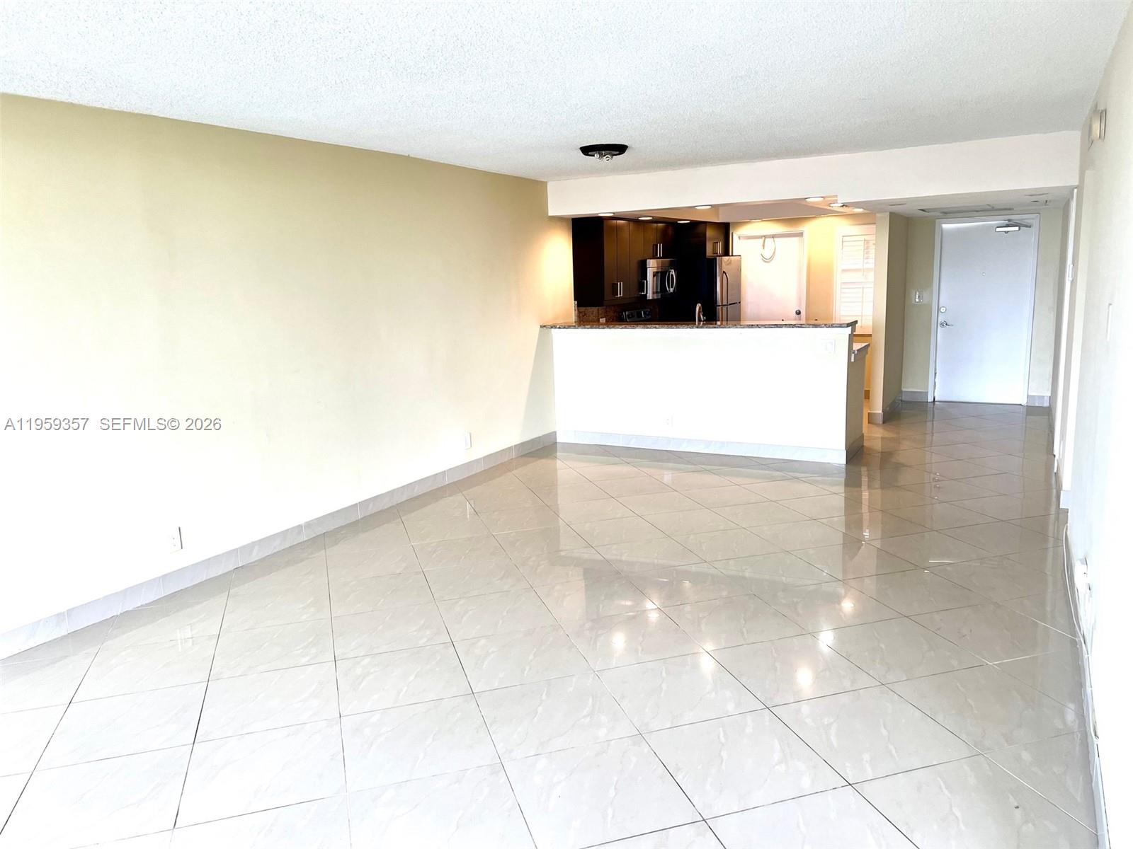 An open-concept living area features light-colored tile flooring and a kitchen with dark cabinetry — 2940 N Course Dr # 910, Pompano Beach FL 33069, POMPANO BEACH, FL