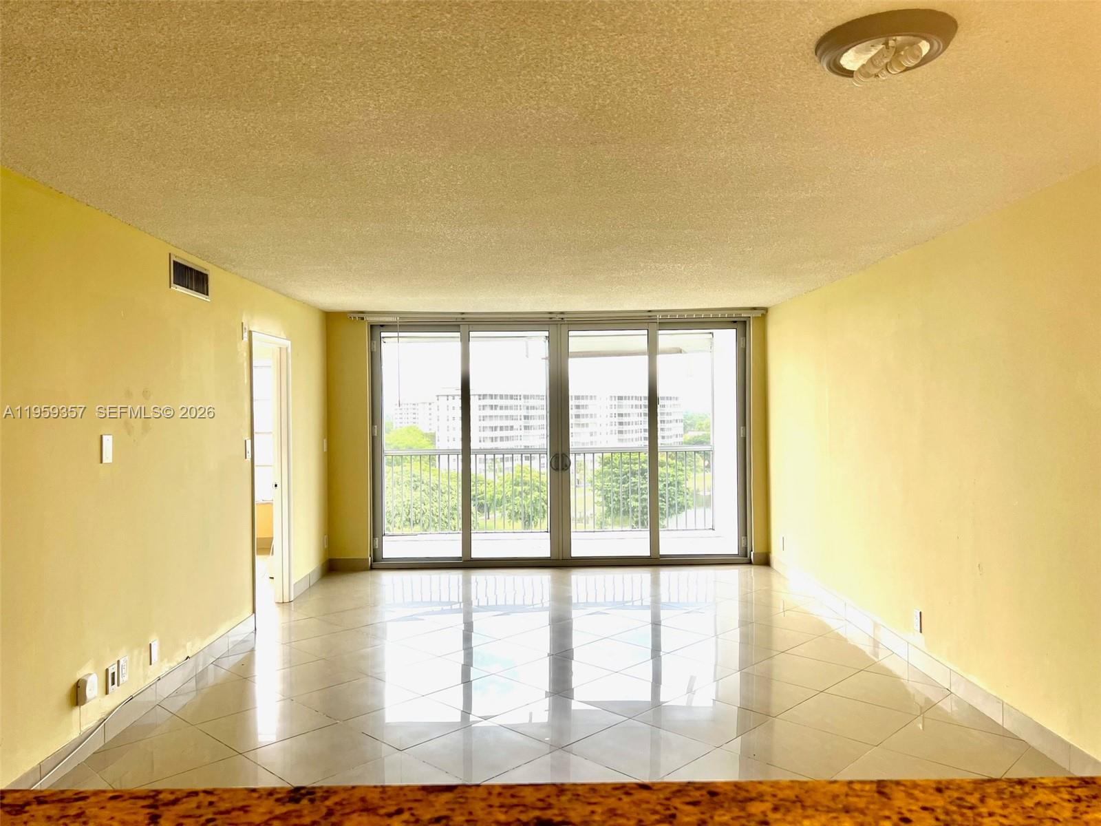 An empty living room with light yellow walls, white tile floors, and a balcony view — 2940 N Course Dr # 910, Pompano Beach FL 33069, POMPANO BEACH, FL