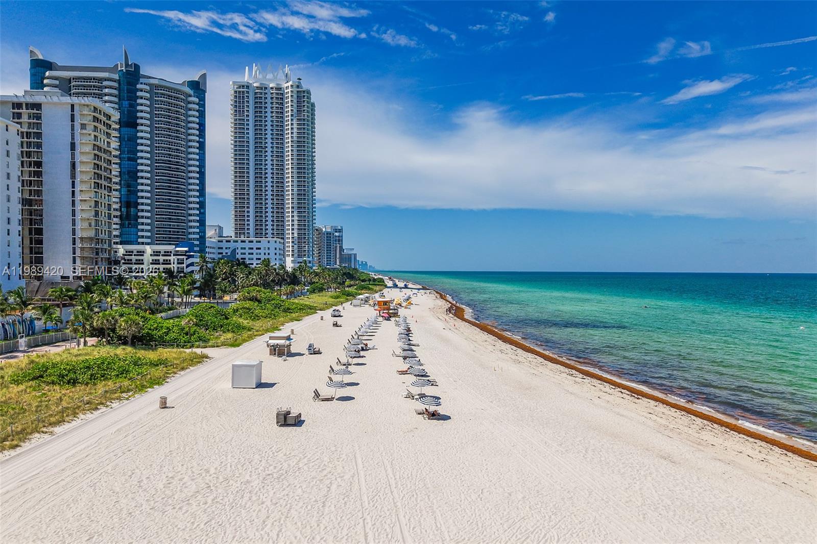 An aerial view shows a sandy beach with lounge chairs alongside tall oceanfront residential buildings — 6039 Collins Ave # 833, Miami Beach FL 33140, MIAMI BEACH, FL