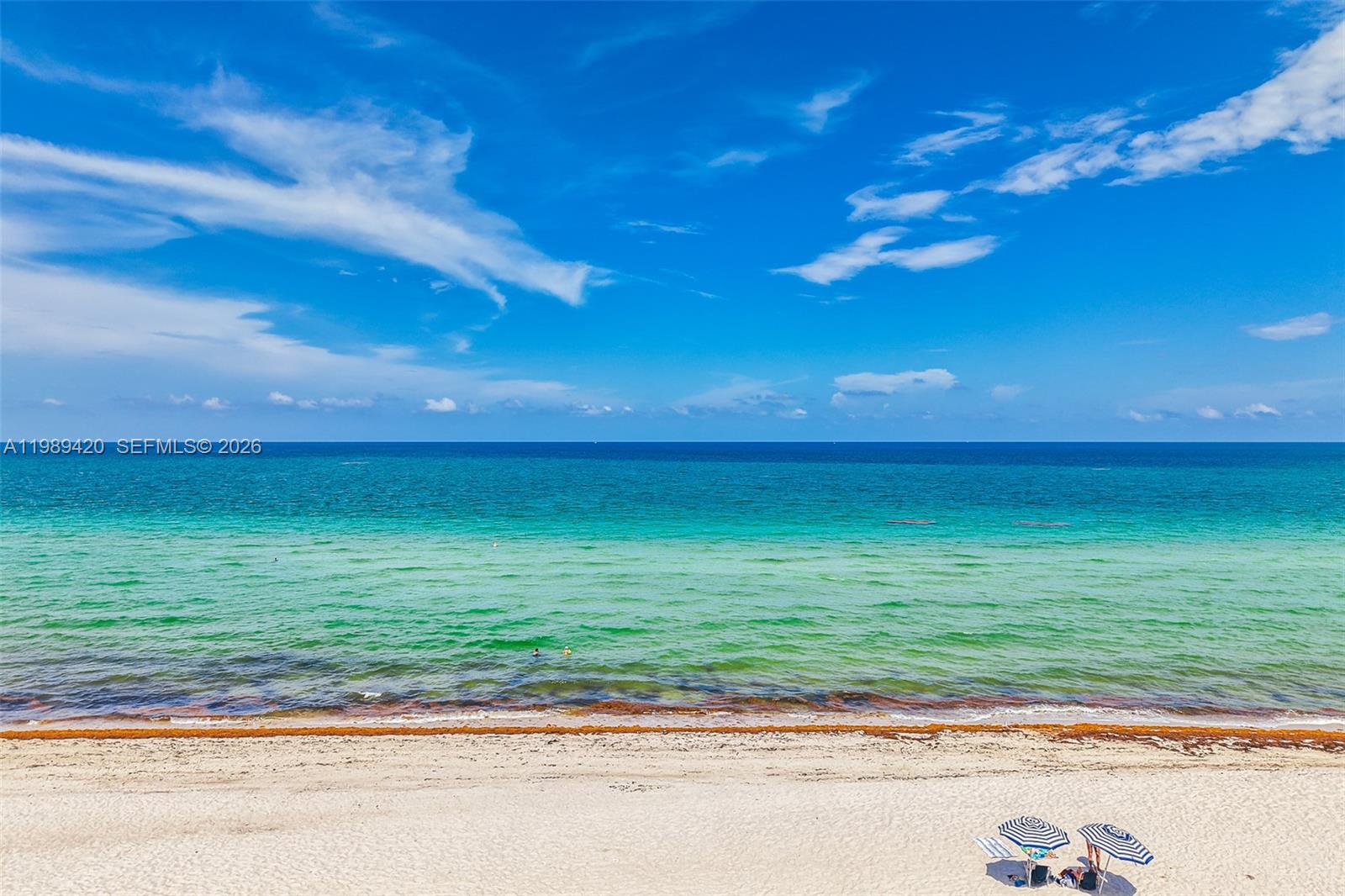An aerial view of a sandy beach with blue ocean water and two striped umbrellas — 6039 Collins Ave # 833, Miami Beach FL 33140, MIAMI BEACH, FL