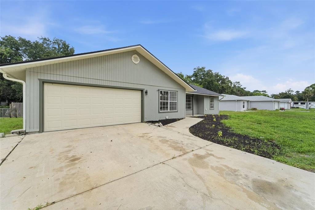 A gray house with a two-car garage and a concrete driveway under a blue sky — 2509 JUNIPER DRIVE, EDGEWATER, FL