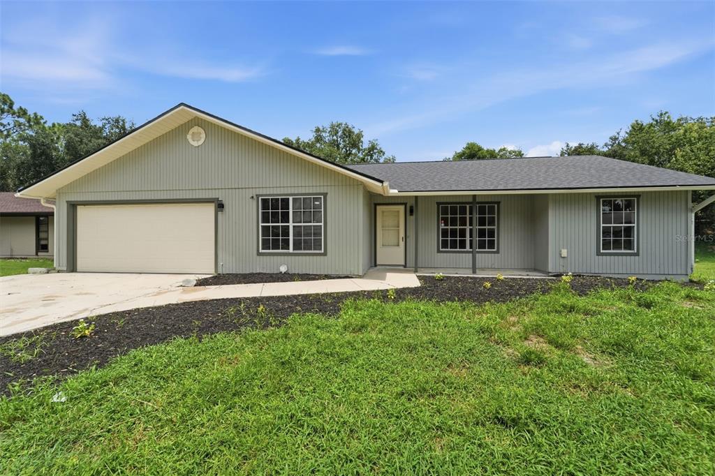 A single-story house with light green vertical siding, a two-car garage, and a covered entryway — 2509 JUNIPER DRIVE, EDGEWATER, FL