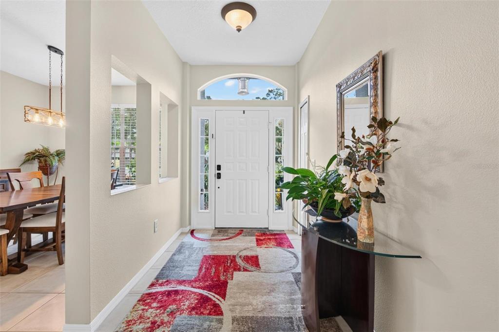A bright entryway features a white front door, a patterned rug, and a glass console table — 2245 MISTY COURT, DUNEDIN, FL