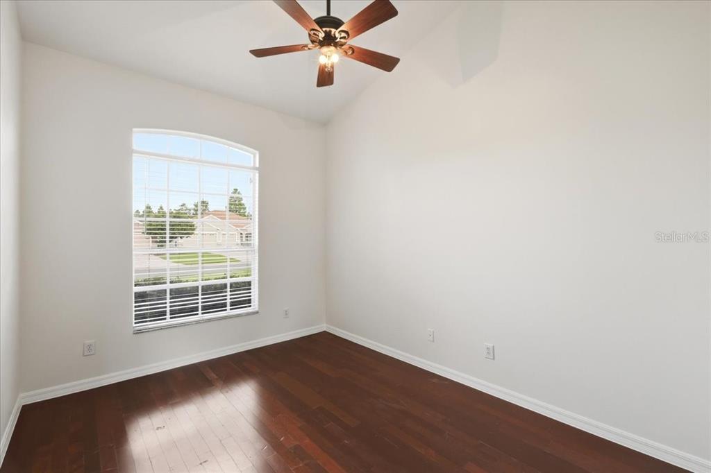An empty room with dark hardwood floors, white walls, and a ceiling fan — 4303 SHOSHONE COURT, ST CLOUD, FL