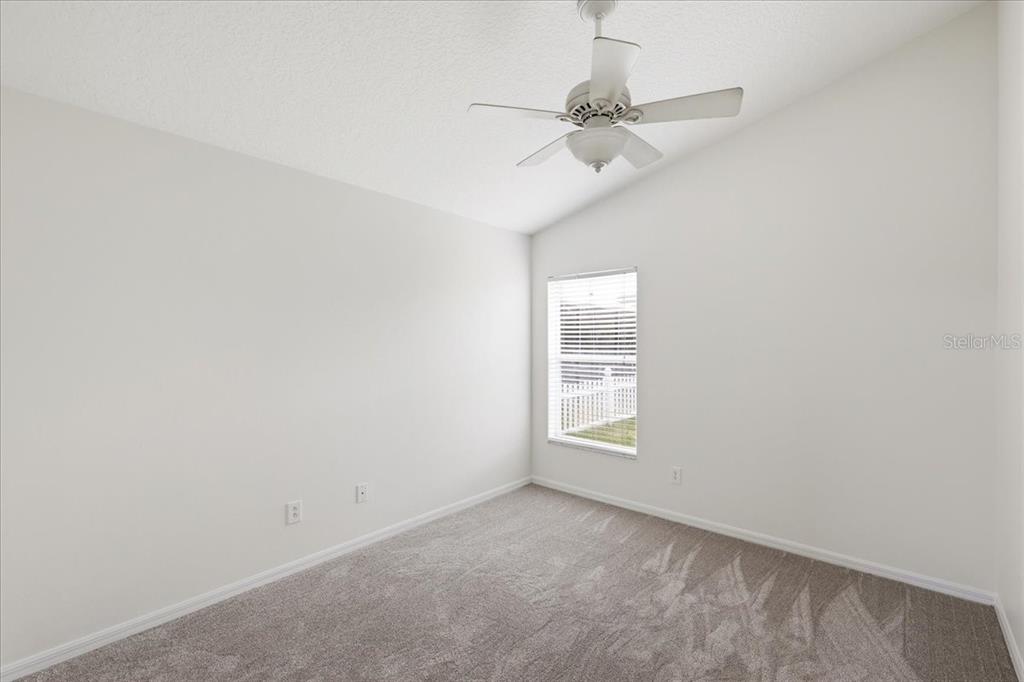An empty bedroom features light gray walls, beige carpeting, a ceiling fan, and a window — 4303 SHOSHONE COURT, ST CLOUD, FL