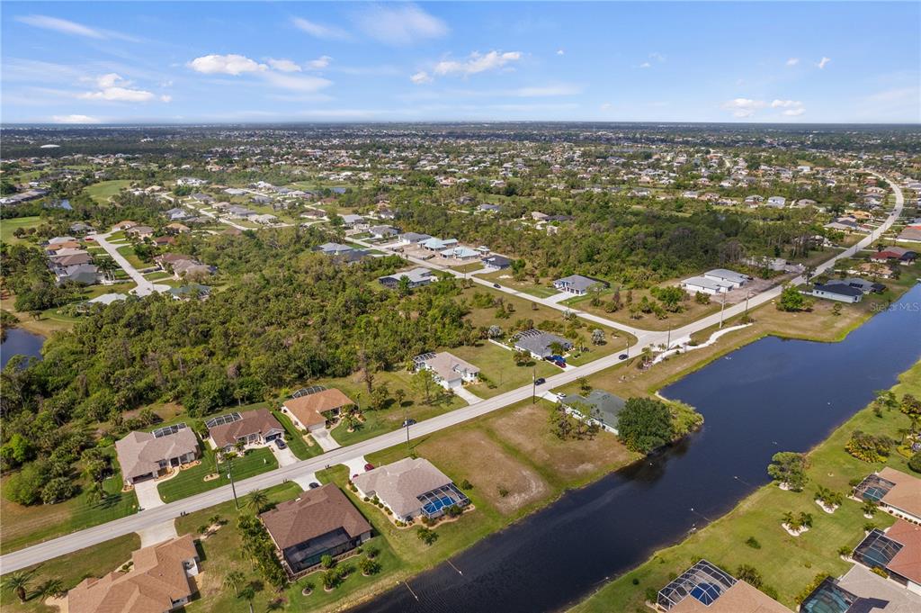 An aerial view shows a suburban neighborhood with houses, a canal, and surrounding wooded areas — 805 ROTONDA CIRCLE, ROTONDA WEST, FL