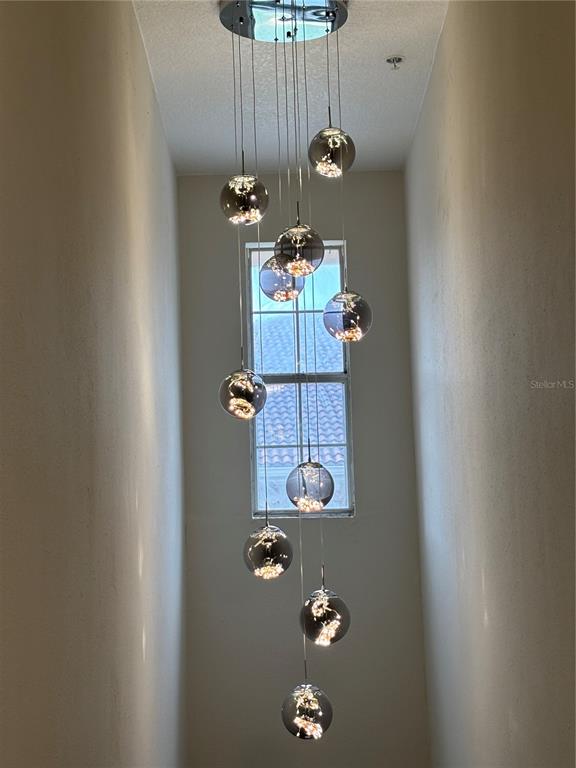A multi-pendant glass globe chandelier hangs in a tall, narrow stairwell with neutral walls — 12208 WILD IRIS WAY UNIT 112, ORLANDO, FL