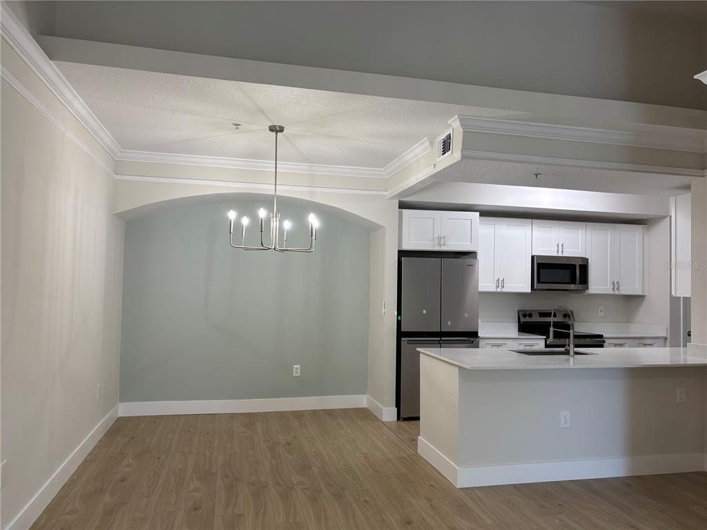 A dining area with a light green accent wall and chandelier adjacent to a kitchen — 12208 WILD IRIS WAY UNIT 112, ORLANDO, FL