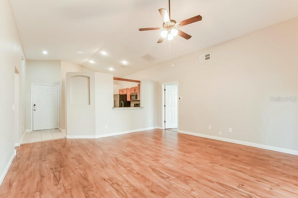 An empty living room with light wood-look flooring, a ceiling fan, and a kitchen pass-through — 4166 SHADOW CREEK CIRCLE, OVIEDO, FL