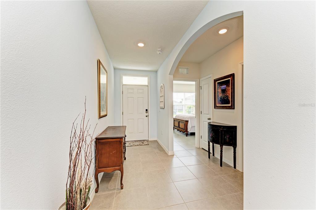 A tiled entryway features a white front door, an arched hallway, and two wooden consoles — 12509 NIGHT VIEW DRIVE, SARASOTA, FL