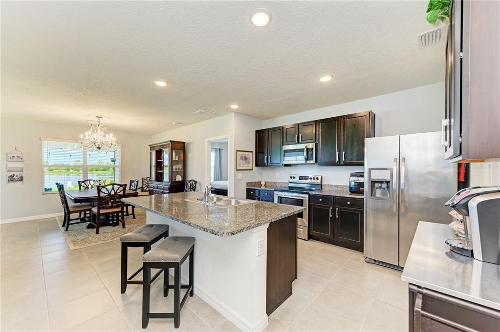 A kitchen with dark cabinets, granite countertops, and an island overlooks a dining area — 12509 NIGHT VIEW DRIVE, SARASOTA, FL