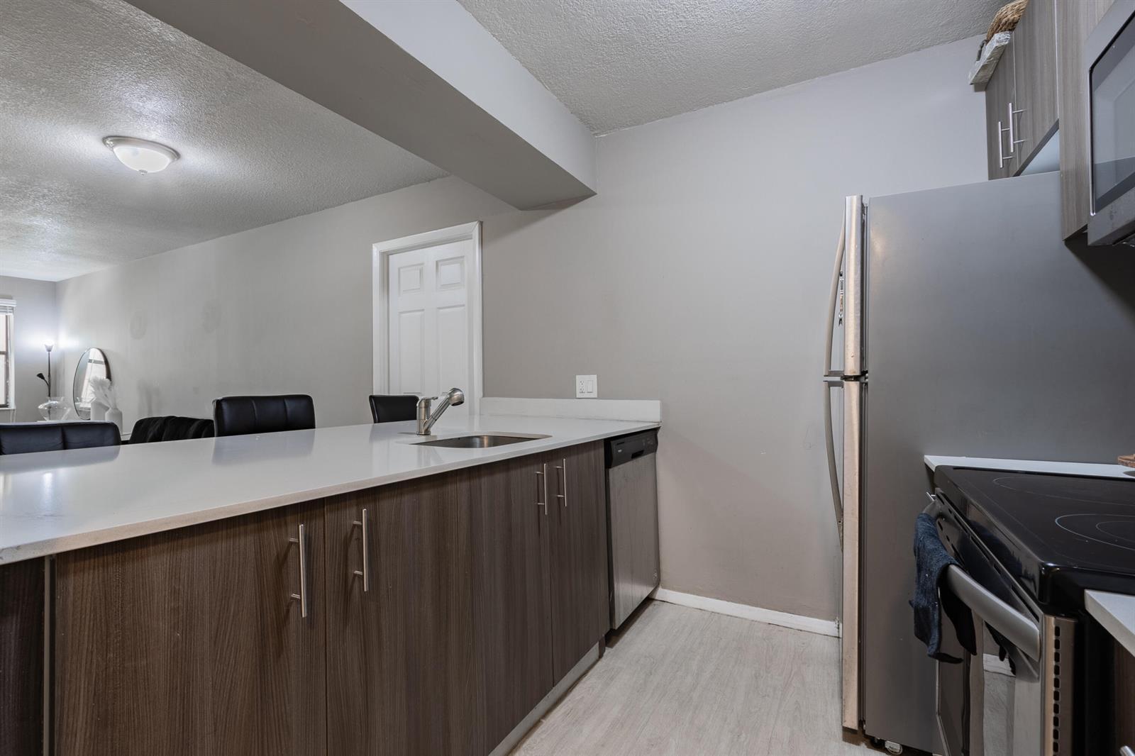 A kitchen features dark wood cabinets, stainless steel appliances, and a white countertop breakfast bar — 8100 Geneva Court # 238, Doral FL 33166, DORAL, FL