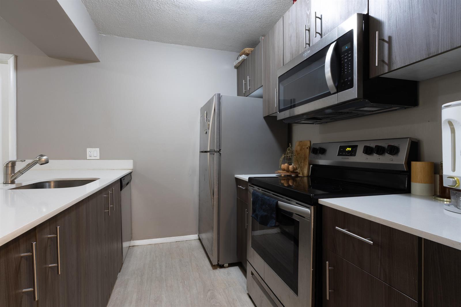 A galley kitchen features dark wood cabinets, stainless steel appliances, and white countertops — 8100 Geneva Court # 238, Doral FL 33166, DORAL, FL