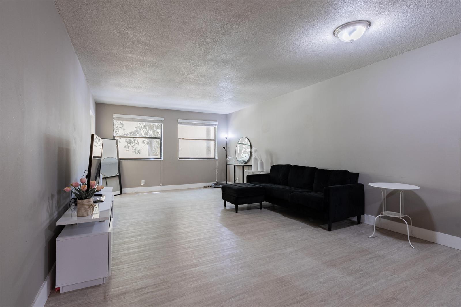 A living room features light wood-look flooring, a black sofa, and a white media console — 8100 Geneva Court # 238, Doral FL 33166, DORAL, FL