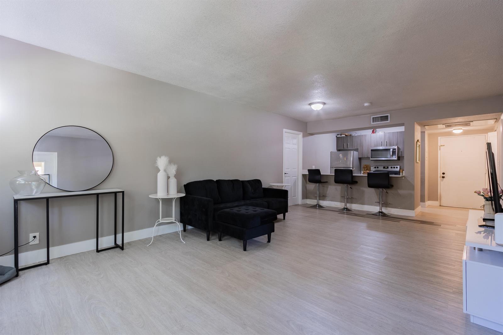 A living room with light wood floors, a black sofa, and an open kitchen area — 8100 Geneva Court # 238, Doral FL 33166, DORAL, FL