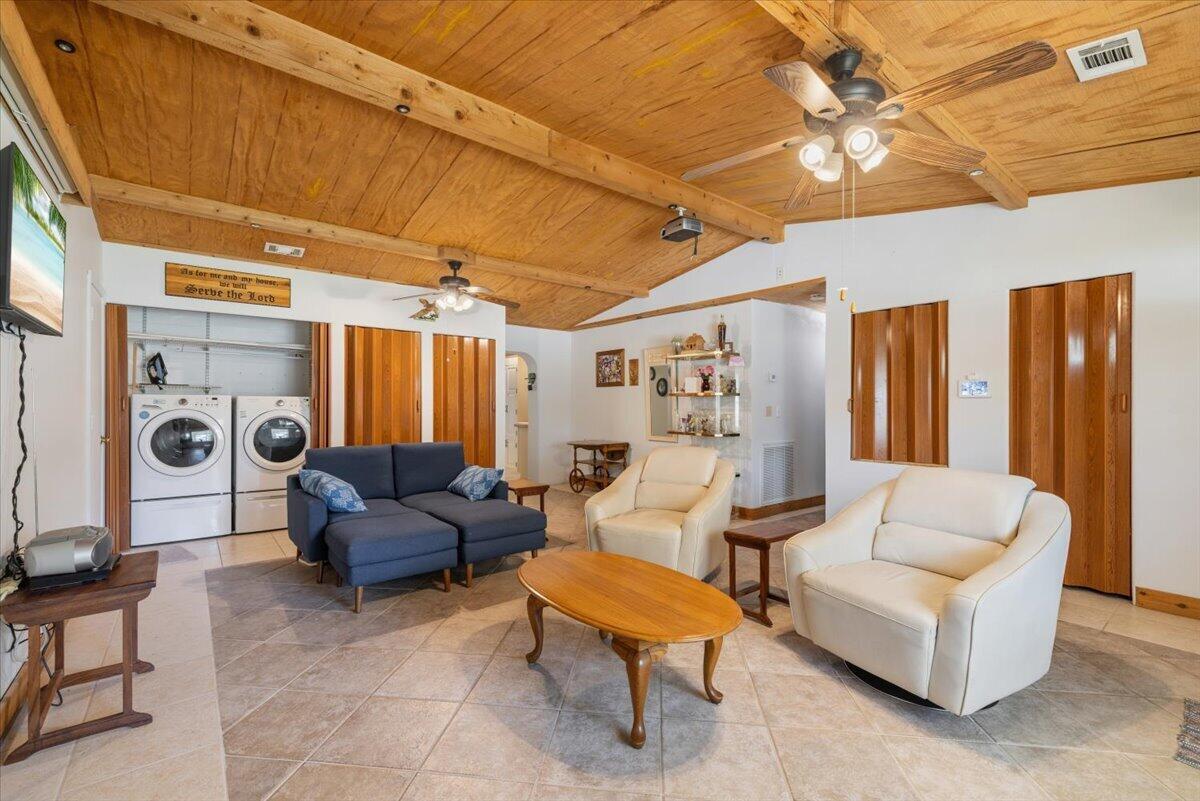 A living room features a wood-paneled vaulted ceiling, tile flooring, a blue sofa, and laundry appliances — 1735 40th Avenue, Vero Beach FL 32960, VERO BEACH, FL
