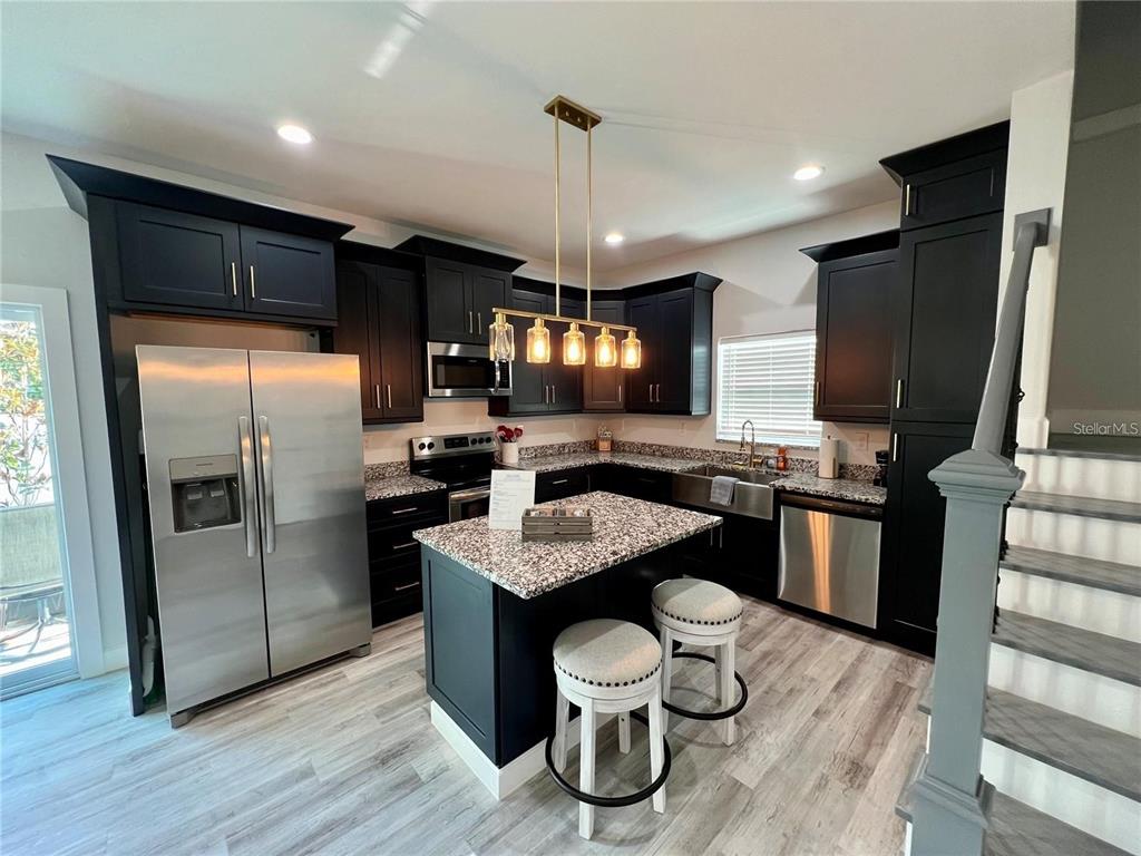 A kitchen features dark cabinets, granite countertops, a central island with stools, and stainless appliances — 5630 QUEENER AVENUE, PORT RICHEY, FL