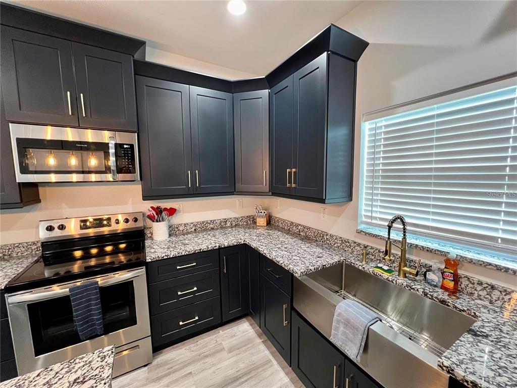 A kitchen features dark blue cabinets, granite countertops, stainless steel appliances, and a farmhouse sink — 5630 QUEENER AVENUE, PORT RICHEY, FL