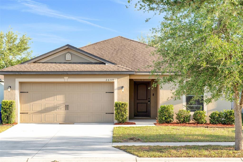 A single-story house with a tan stucco exterior, a two-car garage, and a front lawn — 2659 ROTHERHAM ROAD, TAVARES, FL