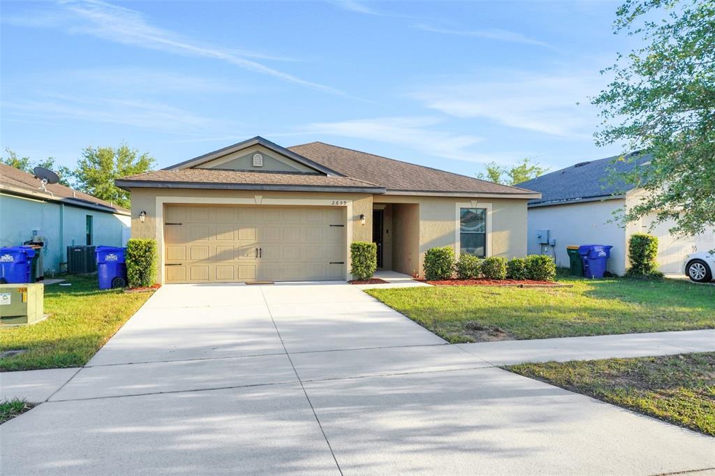 A single-story suburban house with a tan stucco exterior, a two-car garage, and a driveway — 2659 ROTHERHAM ROAD, TAVARES, FL