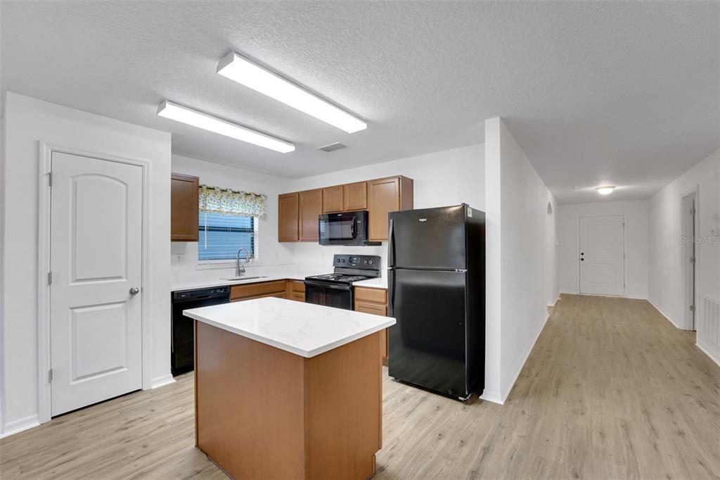 A kitchen features wood cabinets, a white island, black appliances, and light wood-look flooring — 2659 ROTHERHAM ROAD, TAVARES, FL