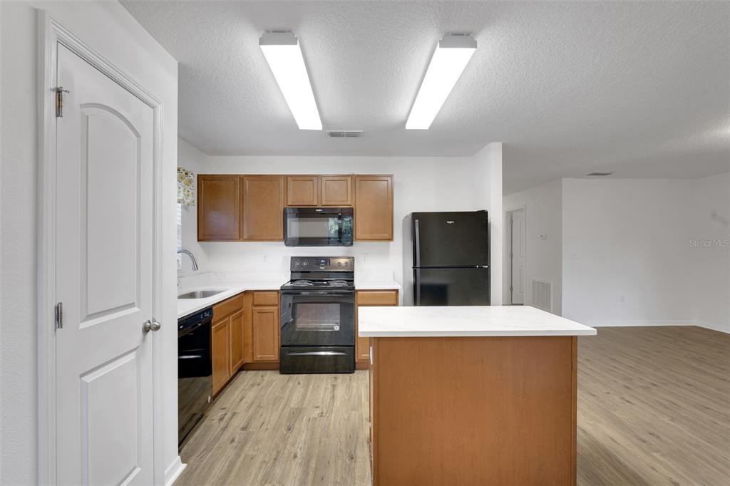 A kitchen with wood cabinets, black appliances, and a white-topped island on wood-look flooring — 2659 ROTHERHAM ROAD, TAVARES, FL